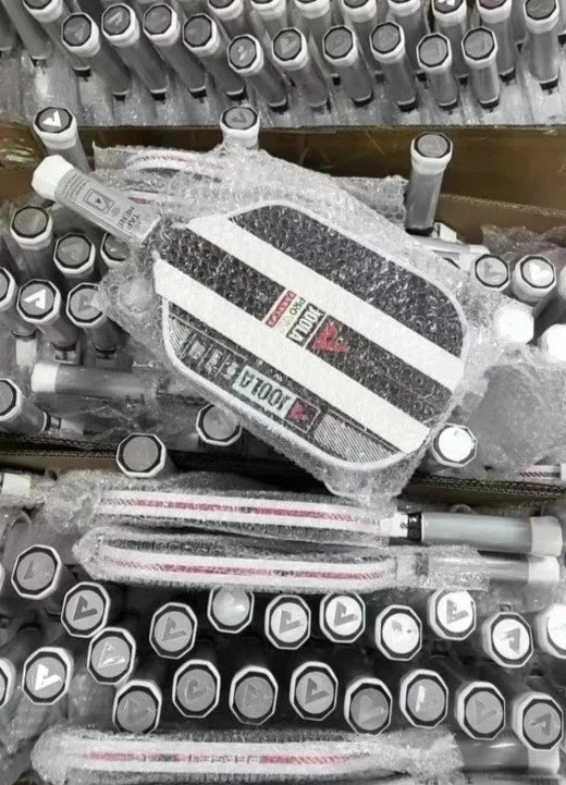 A close-up of a black and white striped electric golf driver wrapped in protective bubble wrap, surrounded by many similar golf clubs stacked in boxes.